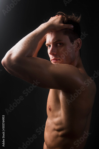 Bodybuilder holds muscular arms on head. Photo in studio on a black background.