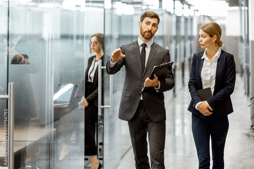 Φωτογραφία Business people walking in the hallway of the modern office building with employees working behind glass partitions