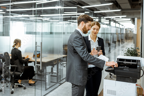 Business man and woman talking near the copier during a coffee break in the hallway of the big corporation photo