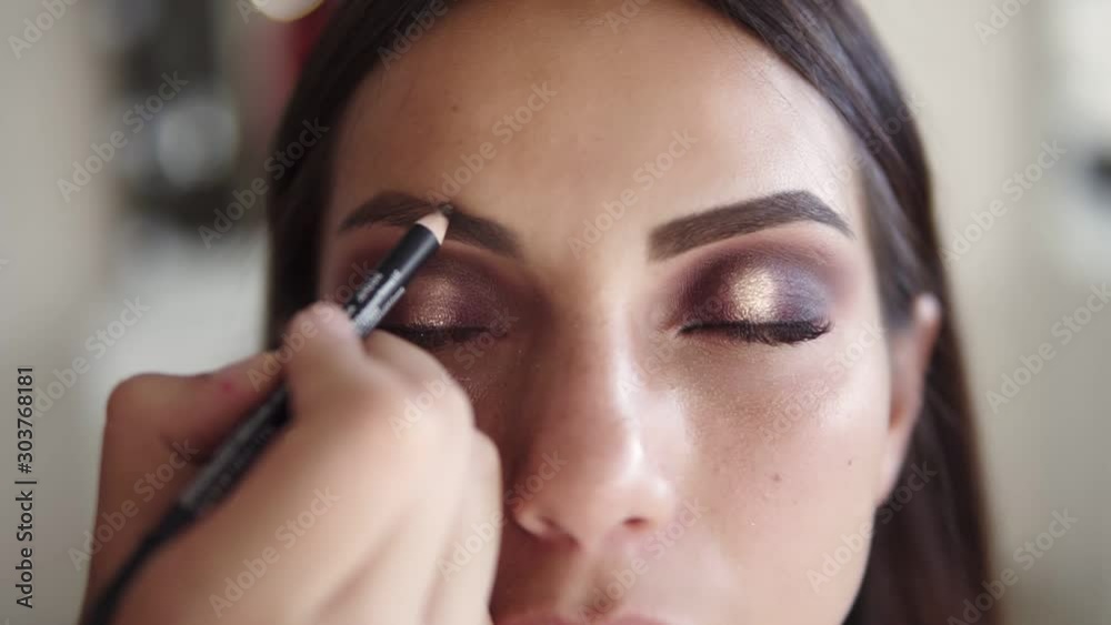 Close up of attractive caucasian model - makeup artist painting with pencil an eye brow line. Shaping eyebrows with cosmetic pencil in beauty studio. Front view Close up of attractive caucasian model - makeup artist painting with pencil an eye brow line. Shaping eyebrows with cosmetic pencil in beauty studio. Front view