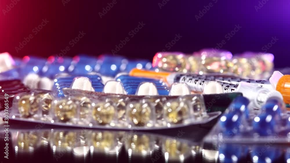 Two syringes lay on different pills, rotation, reflection, macro, on black, back light red and blue Two syringes lay on different pills, rotation, reflection, macro, on black, back light red and blue
