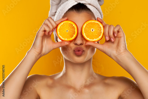 Young beautiful woman with towel on her head holding slices of orange in fron...