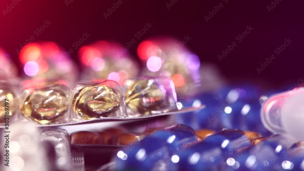 Top of syringe lays on different pills, rotation, reflection, close up, on black, back light red and blue Top of syringe lays on different pills, rotation, reflection, close up, on black, back light red and blue