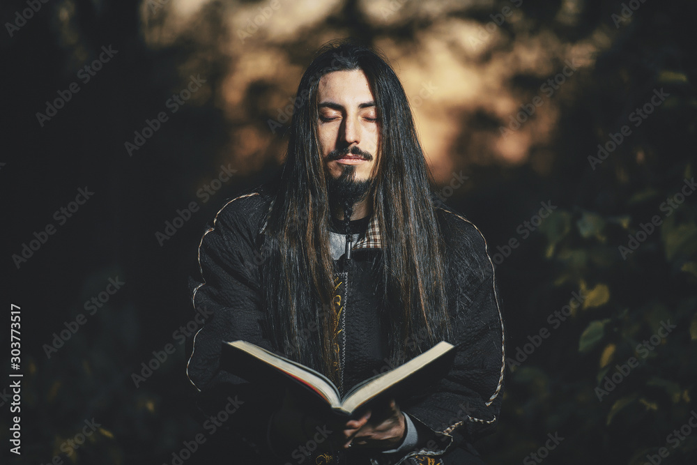 Φωτογραφία A man with long hair and beard in a black cloak in the image of a sorcerer warlock on Halloween