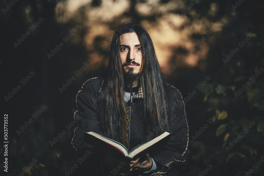 Φωτογραφία A man with long hair and beard in a black cloak in the image of a sorcerer warlock on Halloween