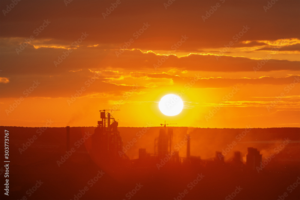 Yellow sunset over industrial landscape with factory chimneys and pipes with smoke polluting the atmosphere.