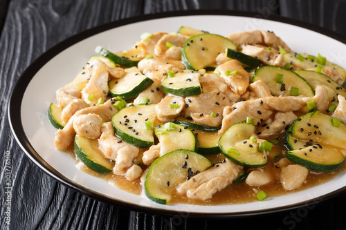 Stir frying chicken fillet with zucchini, sesame seeds and onions close-up on a plate. horizontal