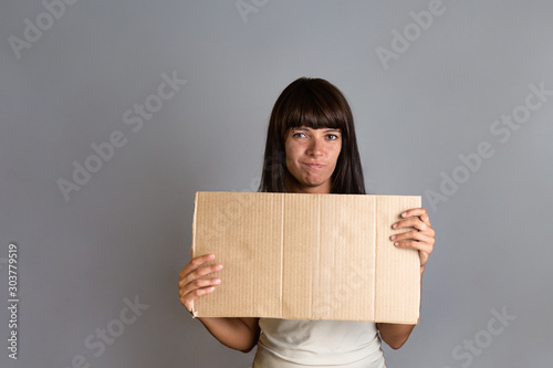 Business and advertising. A young brunette woman with a piercing, holding a cardboard. Gray background. Copy space