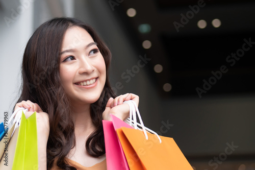 happy woman shopping looking up and holding shopping bag in shopping mall or shopping center; concept of buying, grand sale, boxing day, celebration sale, discount, good deal for woman shoppers