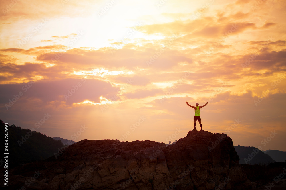 Successful man raising hands on the cliff with the golden sky background,Trail runner on the mountain,Business background