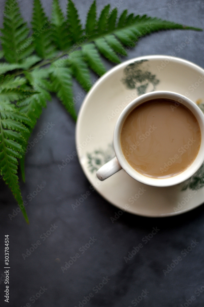 Selective focus a cup of coffee milk and fern leaf over the rustic black background Selective focus a cup of coffee milk and fern leaf over the rustic black background