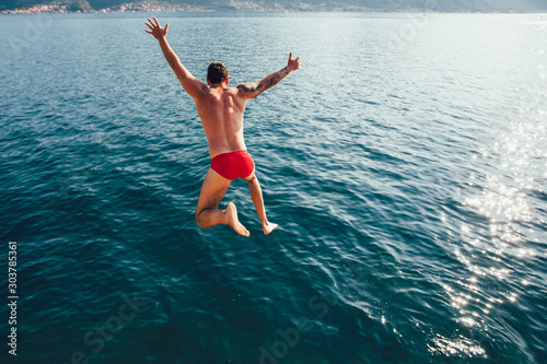 Young man jumping from a rock into the sea.