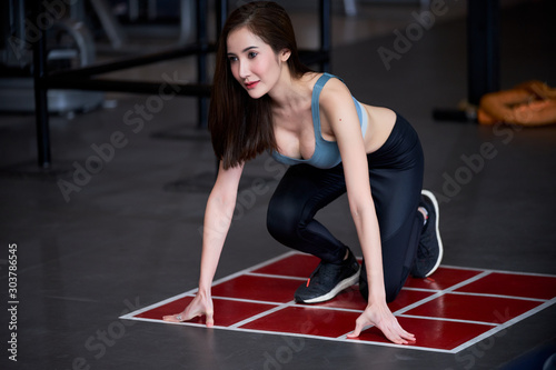 A young beautiful woman is in sprint start pose for training in a gym.