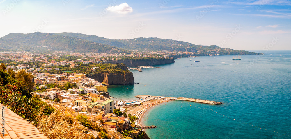 Naklejka premium Panorama of high cliffs, Tyrrhenian sea bay with pure azure water, floating boats and ships, pebble beaches, rocky surroundings of Meta, Sant'Agnello and Sorrento cities near Naples region