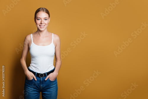 Smiling woman wearing blue jeans and white shirt standing on yellow background