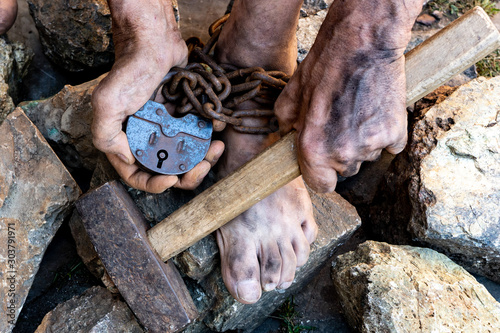 The dirty hands of a slave hold a hammer among the stones. Slave hard labor in the quarries. The symbol of slave labor. photo