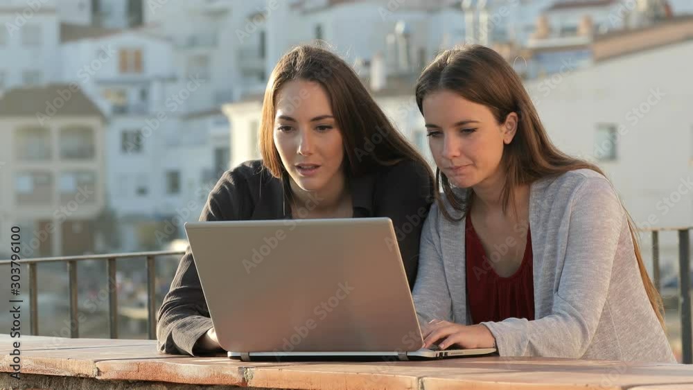 Two amazed friends checking laptop content standing in a balcony in a rural town Two amazed friends checking laptop content standing in a balcony in a rural town