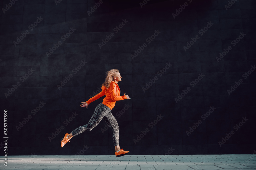 Beautiful slim attractive caucasian woman in sports clothing and with curly hair running outdoors.