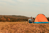 Young couple on a camping holiday, they siting in front of the tent talking and relaxing.