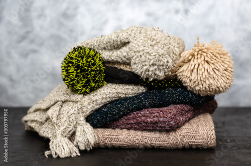A stack of folded knitted winter scarves and hats on gray background. Season of warm clothes. Time to keep warm. Closeup