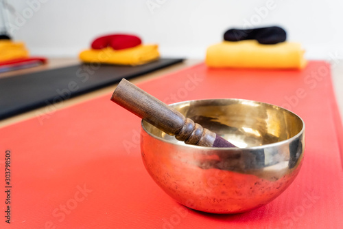 Bronze singing bowl with clapper on red yoga mat for meditation or massage (shallow depth of field)