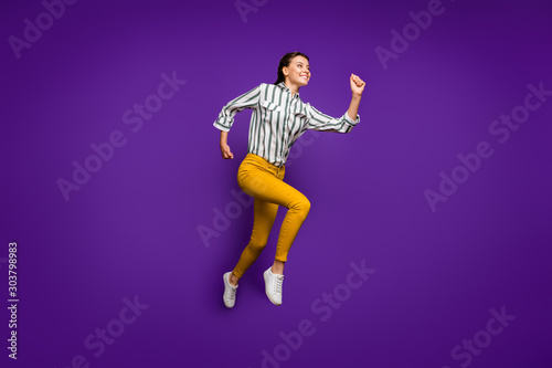 Full size profile photo of crazy beautiful lady jumping high rushing to finish line competitive sportswoman wear striped shirt yellow trousers isolated purple color background