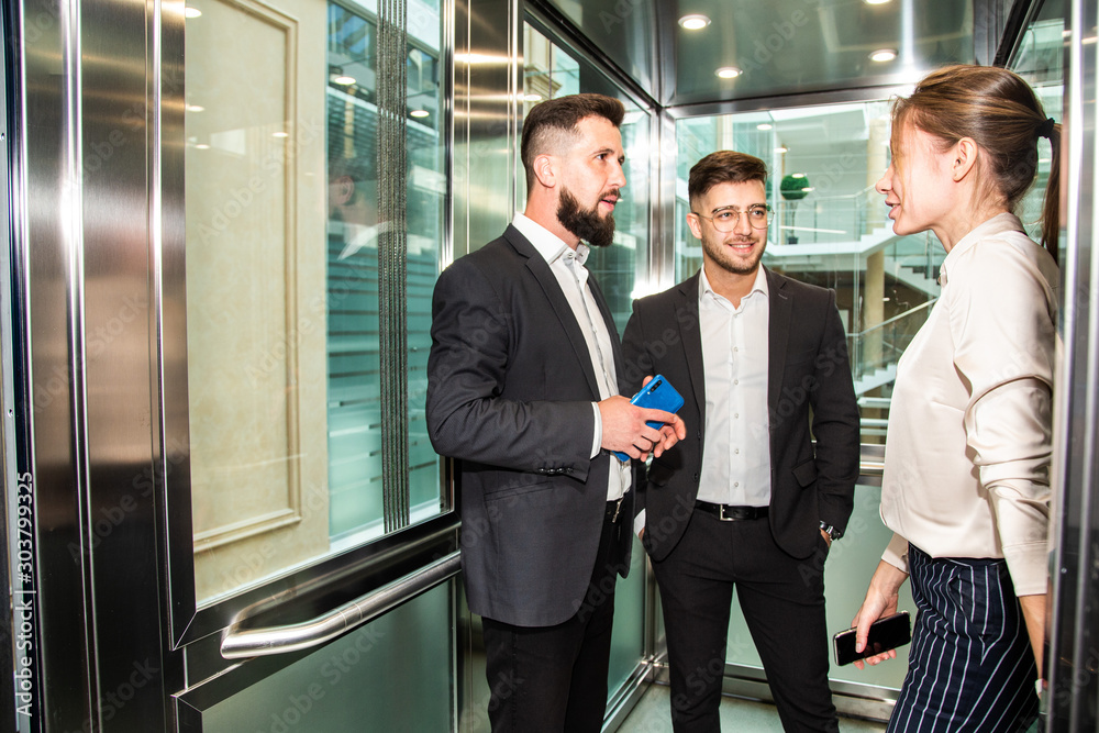 Business team group going on elevator. Business people in a large glass elevator in a modern office. Corporate businessteam and manager in a meeting. Business team group going on elevator. Business people in a large glass elevator in a modern office. Corporate businessteam and manager in a meeting.