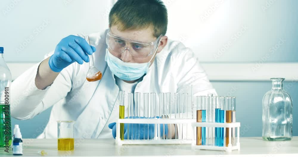 Scientist in the Laboratory Holds a Flask with Toxic Liquid and Inspects it. Man Shakes a Flask in a Lab Room. Research of Chemicals. Close up 4k. Scientist in the Laboratory Holds a Flask with Toxic Liquid and Inspects it. Man Shakes a Flask in a Lab Room. Research of Chemicals. Close up 4k.