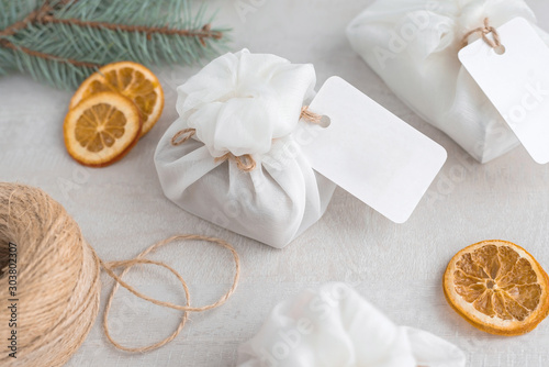 Christmas presents wrapped with white furoshiki fabric, labels and dried orange slices. Eco friendly gift.
