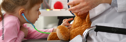 Little girl hold in arms toy stethoscope playing with teddy bear