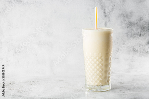 Banana oats smoothie or vanilla milkshake in glass on bright marble background. Overhead view, copy space. Advertising for milkshake cafe menu. Horizontal photo.