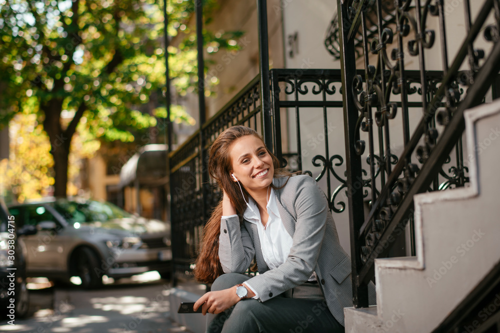 Fototapeta premium Young businesswoman outside. Beautiful businesswoman outdoors listening music. 