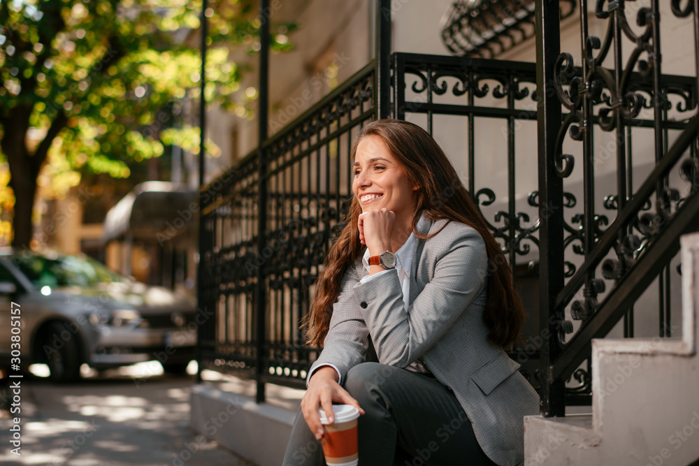 Young businesswoman outside. Beautiful woman drinking coffee while sitting on stairs. 