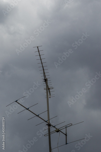 An antenna stands isolated on top of a building against a sky with dark storm clouds image in vertical format with copy space