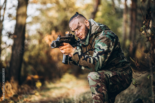 Portrait of a camouflage soldier with rifle and painted face playing airsoft outdoors in the forest