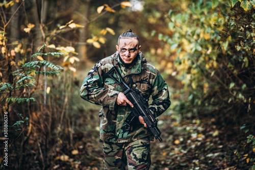 Portrait of a camouflage soldier with rifle and painted face playing airsoft outdoors in the forest © bedya