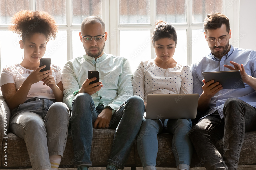 Concentrated diverse people sitting together on sofa, using different gadgets. Concentrated diverse people sitting together on sofa, using different gadgets.