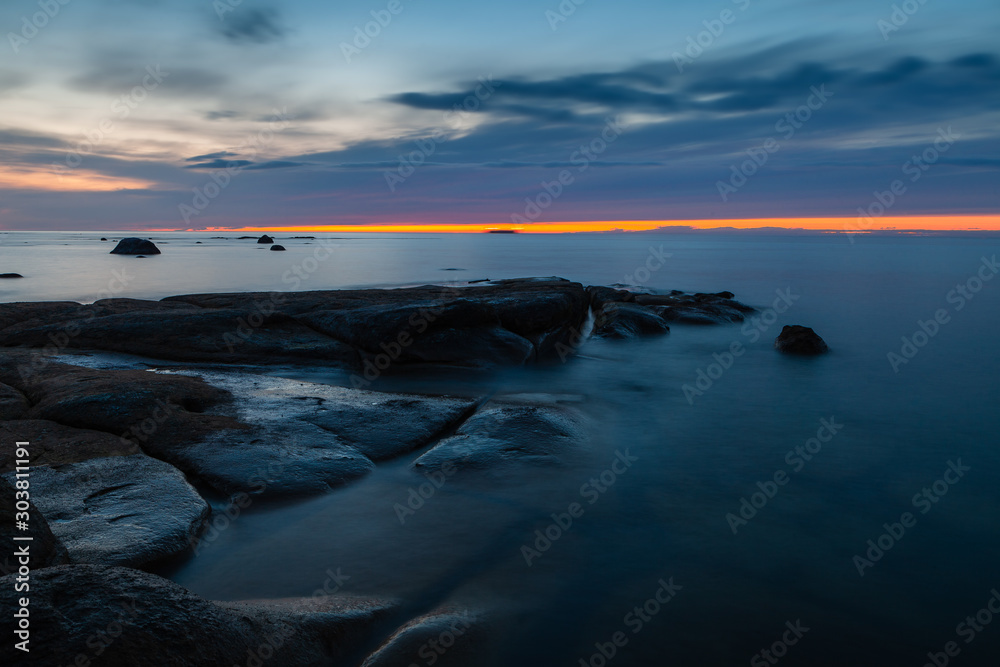 Sunset sky over stones and flat rock sinking under Baltic sea. Amazing wilderness of Estonia.