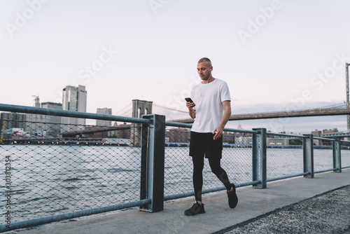 Young sportsman with earphones and smartphone against modern city