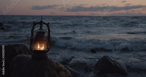 Oil lantern burning on rock in sea water at sunset