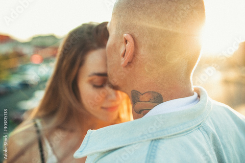 Tenderness. Tanned young caucasian couple, modern lovestory in film grain effect and vintage style. Sunset time. Walking on the city's street, summer evening. Honeymoon concept. Toned in teal orange.