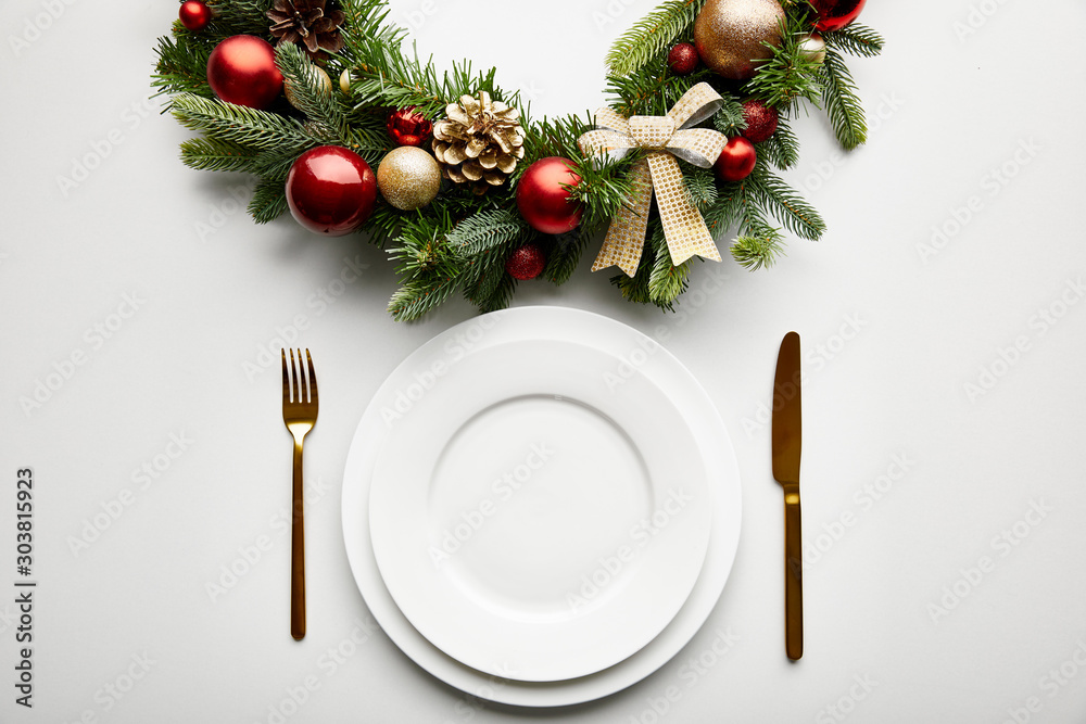 Φωτογραφία top view of white plates with golden cutlery near festive Christmas wreath with