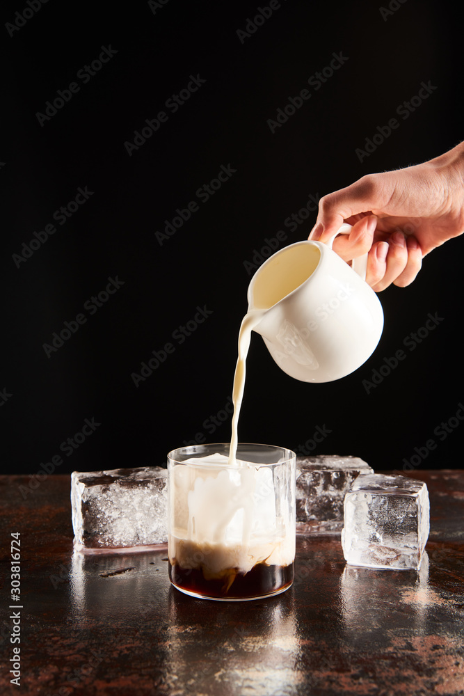 Φωτογραφία cropped view of woman poring milk in glass with ice cubes isolated on black