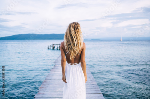 Seductive shapely female in light dress standing on pier