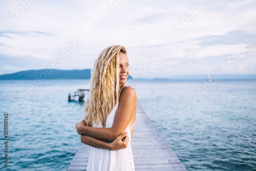Smiling fit female in light dress standing on boardwalk