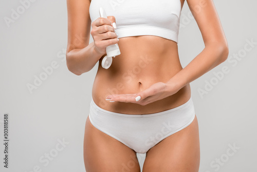 cropped view of slim woman in underwear squeezing lotion isolated on grey
