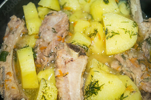 Stewed pork ribs with potatoes, onions, carrots and dill in a saucepan. Close up. Traditional recipe. Home cooking.