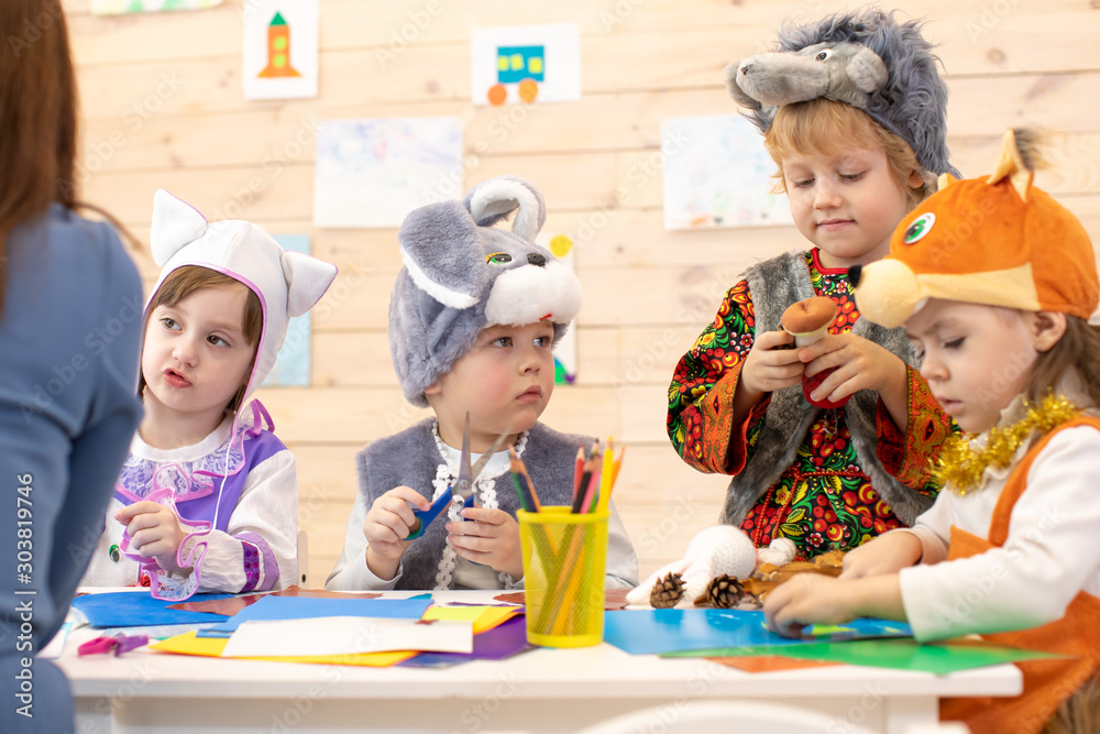 Kids with teacher make hands crafts in kindergarten. Children prepare to christmas holiday. Group of preschoolers on lesson in classroom - obrazy, fototapety, plakaty 