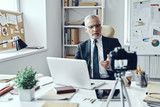 Senior man in elegant shirt and tie working using laptop while making social media video