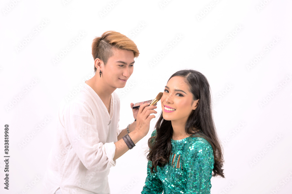 Professional male make up artist applying color brush on beautiful young asian woman model face with smiling happy on white background, Isolated.